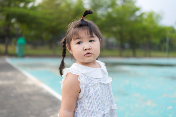 一位穿着白色连衣裙的可爱亚洲小女孩站在户外的游乐场上，在克罗地亚绽放公园的背景下，小女孩快乐地微笑着，高清照片。图片下载