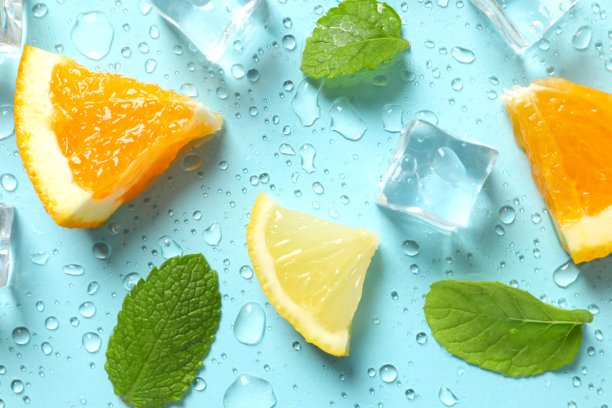 俯视角度拍摄的薄荷叶、橙子片、柠檬片、冰块和水滴在淡蓝色背景上的照片图片下载