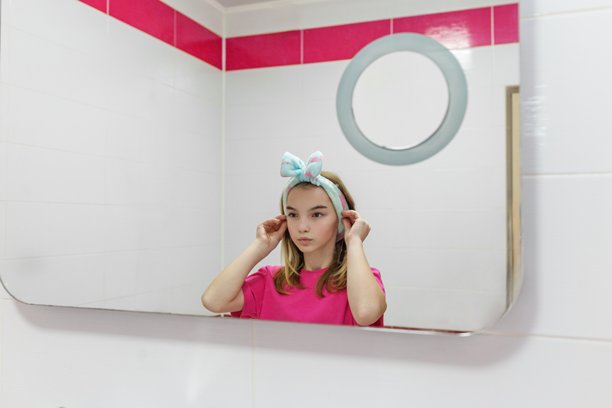 年轻女孩在浴室镜子前调整蝴蝶结发带。早晨卫生习惯概念。图片下载