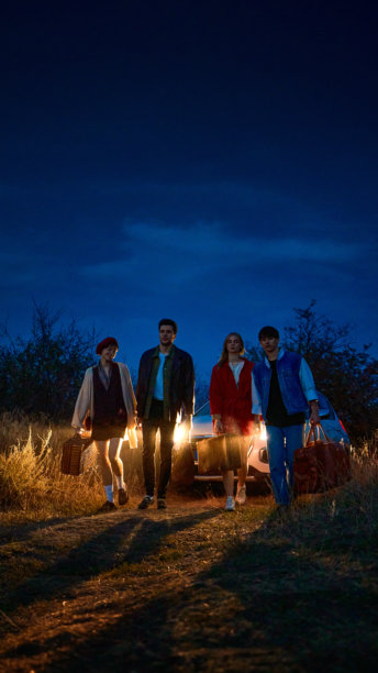 朋友们带着行李在夜晚走动，身后来了一辆复古汽车，车灯闪耀图片下载