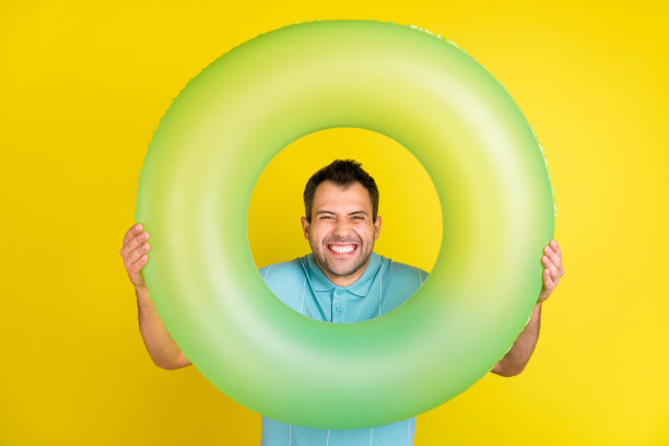 照片：一个滑稽的棕色头发男子，穿着蓝色T恤，手持圆圈，孤立在黄色背景上图片下载