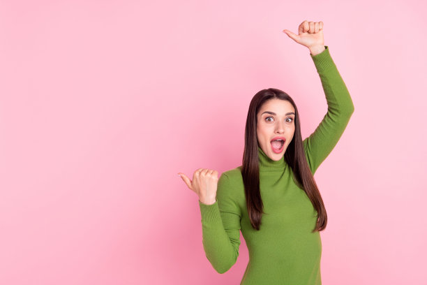 照片：惊讶的年轻女子手指着粉红色背景上的空白空间，传递信息图片下载