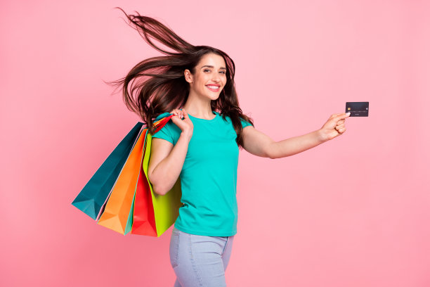 年轻女子侧面照片，开心积极地微笑，手持银行卡，在柔和的彩色背景上购物支付，孤立。图片下载