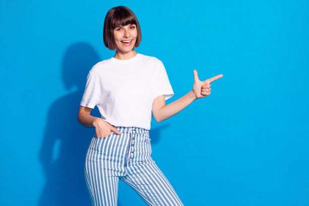 照片肖像：留着波波头的漂亮女孩，穿着休闲装，面带微笑，伸出手指，有复制空间，背景是鲜艳的蓝色。图片下载