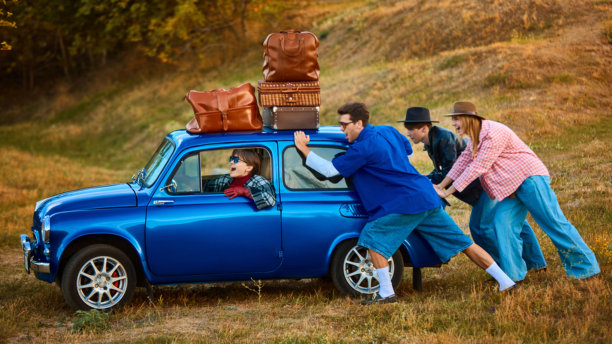 朋友们推着载有行李的复古蓝色汽车，一位女士在驾驶时笑着图片下载