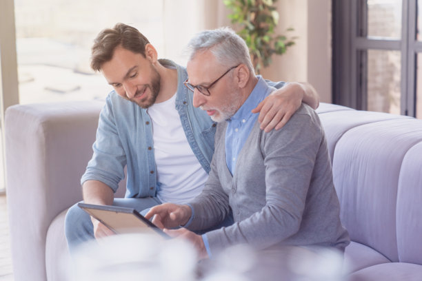 一个充满爱心的成年儿子在家里拥抱他年迈的父亲，父亲正展示着家庭照片，讲述着年轻时的故事。父亲节快乐！我爱你，爸爸！图片下载