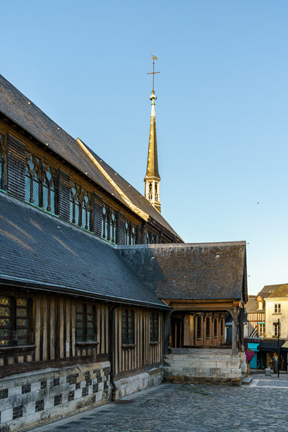 法国诺曼底小镇翁弗勒（Honfleur）一座老木建筑的一部分。照片拍摄于傍晚。建筑附近有一座尖塔，塔顶有十字和公鸡装饰。图片下载