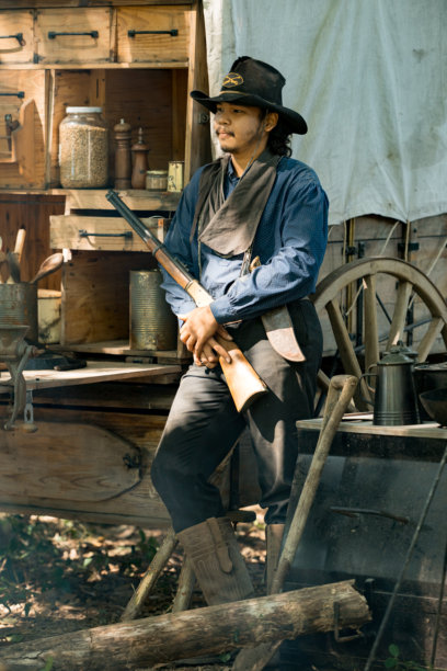 一名牛仔站在森林营地，手持步枪，阳光穿过烟雾洒落图片下载