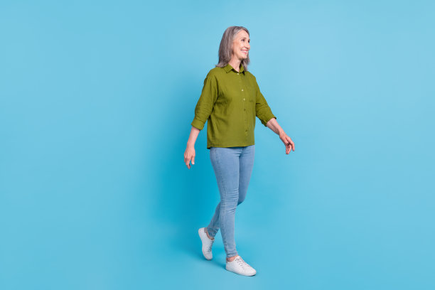 穿着绿色衬衫、牛仔裤和鞋子的奶奶的个人资料照片，她正在旅行，背景是蓝色的，有空白空间。图片下载