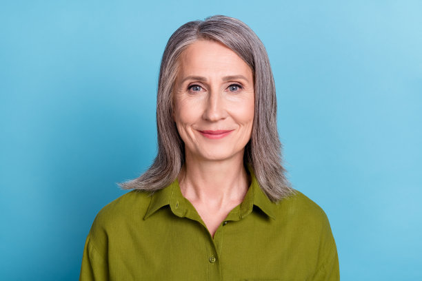 照片：一位积极、开朗、有魅力的奶奶，看着镜头微笑，穿着绿色衬衫，背景是蓝色的。图片下载