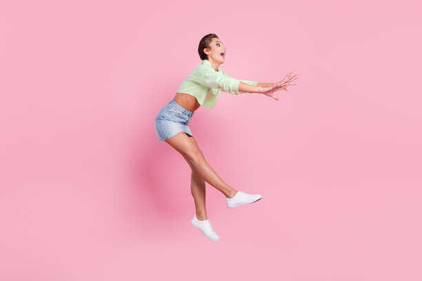 年轻女孩全身侧面照片，惊喜震惊地跳起飞在空中接球，孤立在柔和色背景上图片下载