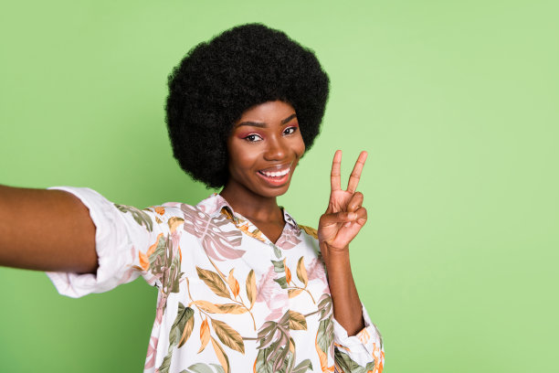 年轻的非洲裔女孩开心地微笑自拍，做出胜利手势，在绿色背景上显得很酷图片下载