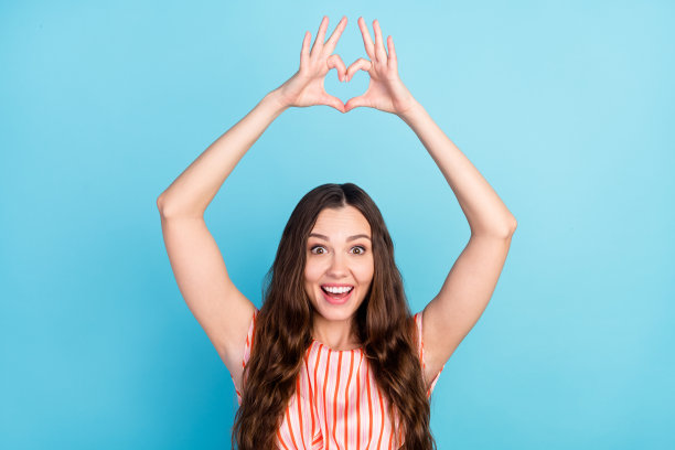 照片：一位深情又兴奋的女士，身穿条纹连衣裙，双手高举，比出爱心手势，背景是孤立的蓝色。图片下载