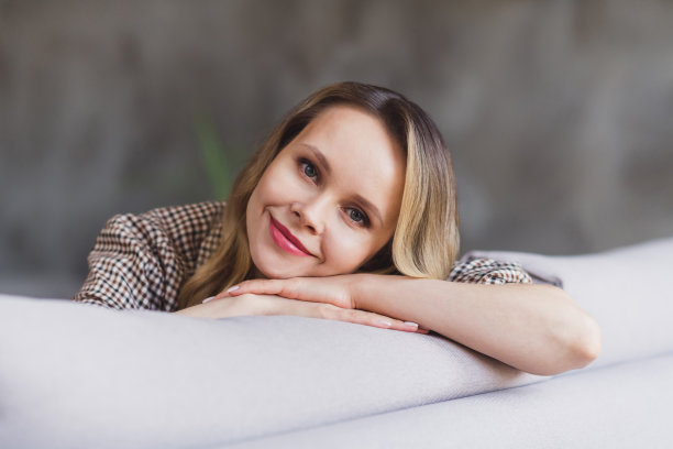 照片：一位乐观的金发女士，戴着棕色夹克，独自在家，手托着头图片下载