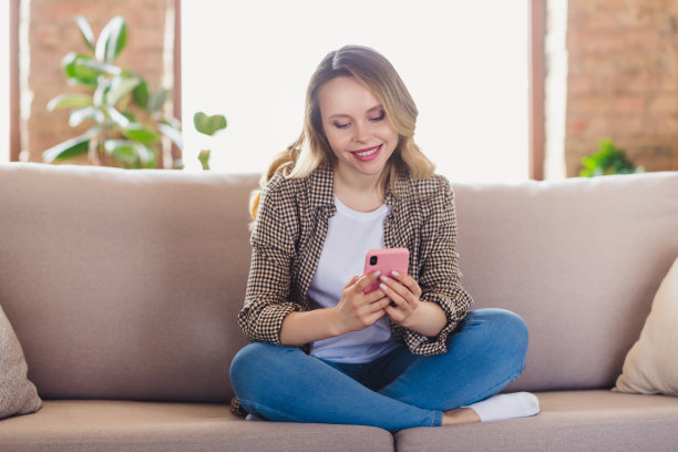年轻女子微笑着坐在沙发上，用智能手机打字的照片肖像图片下载