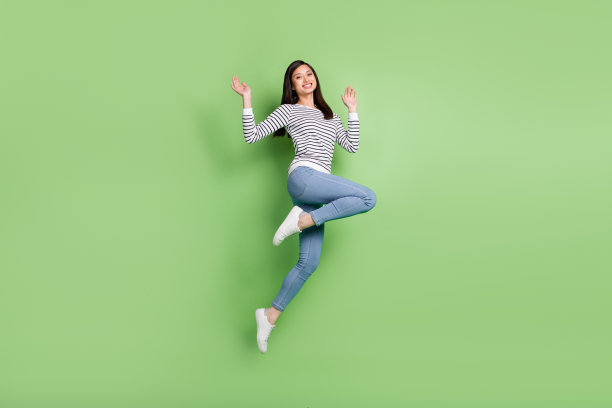 穿着衬衫牛仔裤的时尚时髦的棕发千禧年女士的全身侧面照片，孤立在绿色背景上图片下载