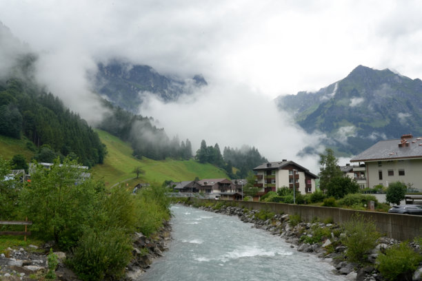 恩格尔贝格的山间河流，两岸有阿尔卑斯风格的房屋，绿色的山坡和低垂的云彩环绕着陡峭的山峰。照片拍摄于2025年7月19日。图片下载