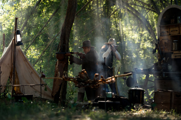 两位牛仔在森林营地瞄准步枪，阳光穿过烟雾洒落图片下载