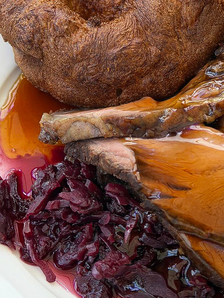 全画幅图片，展示了盛有周日烤肉晚餐的盘子，包括烤牛肉片、约克郡布丁、红卷心菜、肉汁，背景为木桌，俯视角度。图片下载