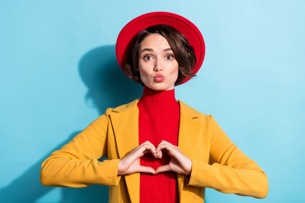 照片：年轻女孩快乐积极地笑着，比出手指爱心手势，表达情人节的爱，孤立在蓝色背景上图片下载