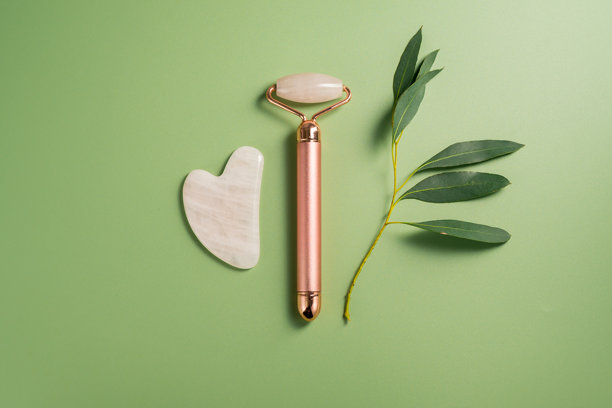 绿色背景上的玫瑰石英刮痧板和面部按摩滚轮，唯美抽象照片。俯视。图片下载