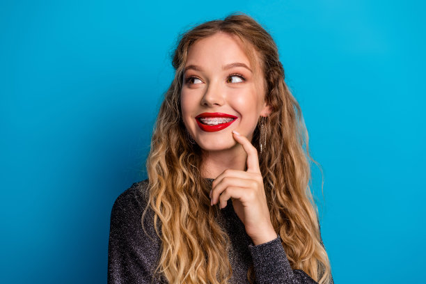 戴着牙套的明媚笑容女子身穿闪亮连衣裙，在蓝色背景前摆姿势，用于美容、时尚和节日素材照片图片下载