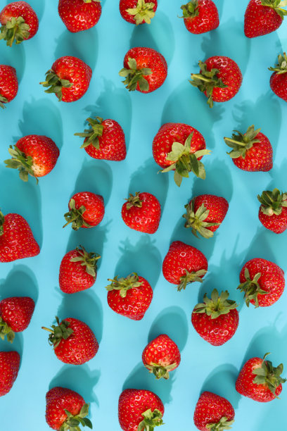 俯视拍摄的满幅照片，展示了新鲜完整的红草莓和绿叶，背景为青蓝色，体现健康与养生概念。图片下载