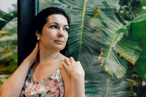 背景有绿叶，一位女子在潮湿的热带玻璃旁摆姿势的照片图片下载