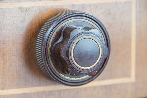 木质表面上的复古相机镜头，背景是旧式管式收音机。圆形黄铜或钢制镜头，带有多个环，可能是可调焦距或光圈。暖棕色和黑色调。图片下载