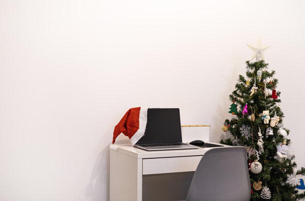 圣诞办公室里戴着圣诞帽的笔记本电脑照片。周末工作，节假日工作，礼物，促销图片下载
