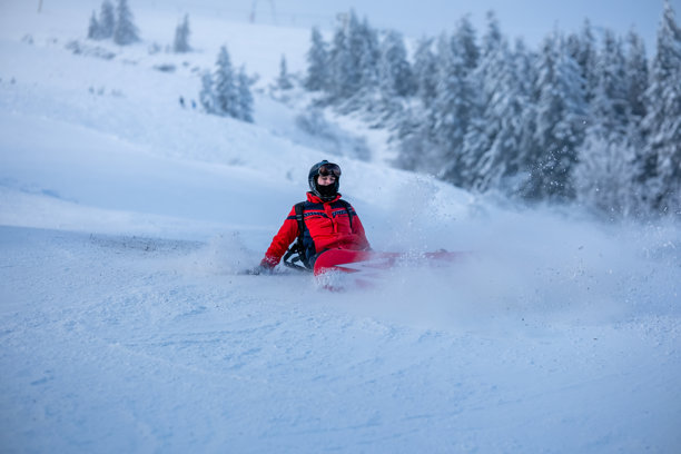2024年12月14日，乌克兰德拉戈布拉特：身穿红色夹克和护目镜的年轻单板滑雪者在粉雪坡上摔倒，在冬季山地运动中滑行并扬起雪花。图片下载