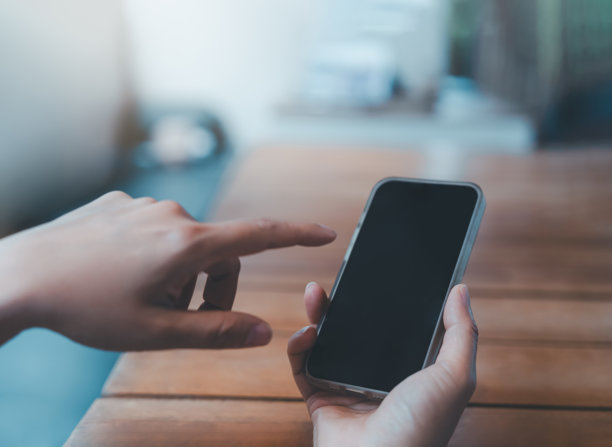 手持智能手机，触摸木桌背景上的空白屏幕，为移动应用模型设计、现代生活方式、在线广告、用户体验演示技术、数字营销展示做准备。图片下载