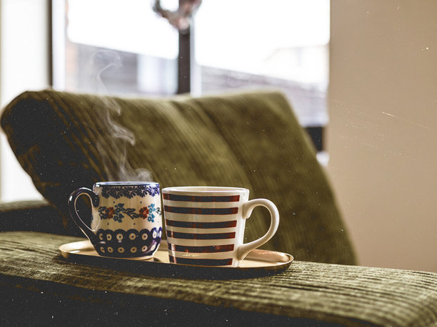 温馨的居家冬日氛围。绿色灯芯绒沙发上托盘里放着两个装有热饮的马克杯，象征着温暖、放松和室内的共享时光。充满复古感的真实家居场景。马克杯里是热茶。图片下载