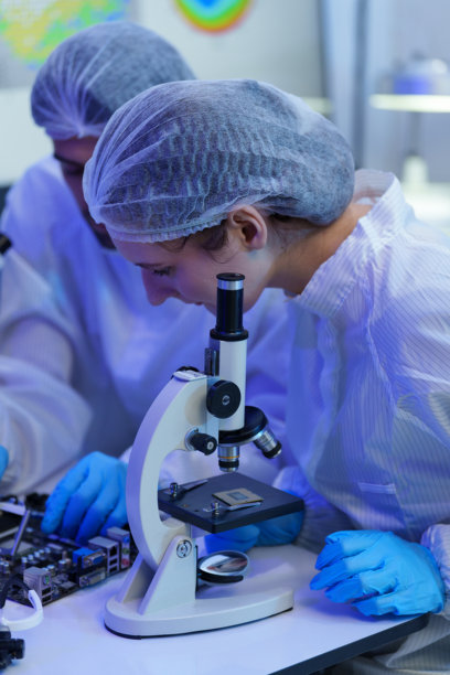 身穿无菌服的国际男女技术人员在半导体制造厂使用显微镜工作（照片）图片下载