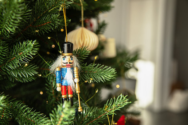 挂在装饰圣诞树上的传统木制胡桃夹子圣诞装饰品，饰有暖色灯光和金色饰球。节日气氛，营造舒适的冬日氛围。图片下载