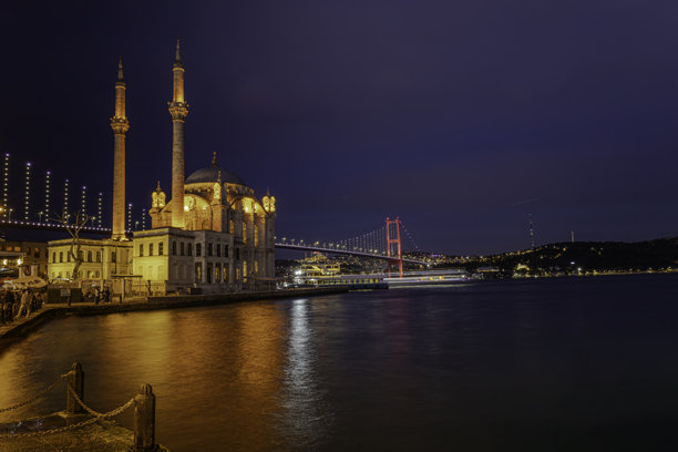 土耳其伊斯坦布尔，博斯普鲁斯海峡大桥作为背景，在蓝色时刻拍摄的、带有两个宣礼塔的奥尔塔科伊清真寺背光照片。图片下载