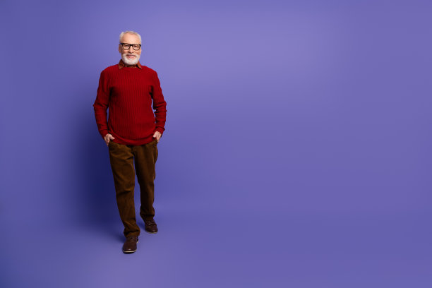 一位穿着红色毛衣的成熟男士，双手插在口袋里，站在紫色背景前，适合生活方式和广告图库照片图片下载