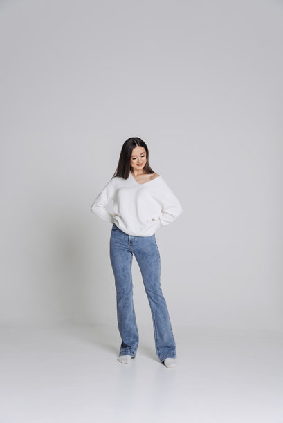 年轻美丽的时尚模特在纯色背景前拍摄的试拍肖像照。身穿白色卫衣和蓝色紧身牛仔裤。全身照图片下载