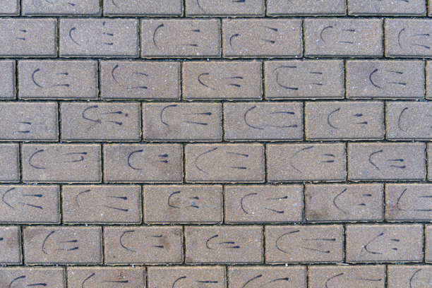 灰色城市人行道的俯视视角。每块水泥砖上都手绘着一张微笑脸的风格化图像。背景纹理。图片下载