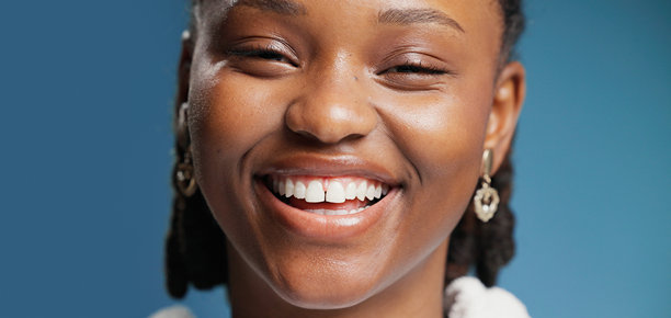 肖像，黑人女性在影棚内微笑进行牙齿美白、口腔护理和卫生。横幅，女性自信地展示清新口气、幸福感和贴面效果，背景为蓝色。图片下载