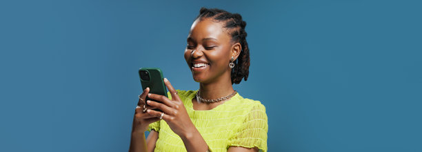 一名非洲女性在工作室里对着手机打字，背景为蓝色，传递出幽默、联系、笑话和信息，并留有样机空间，展示了在线幽默、沟通和APP的使用。图片下载