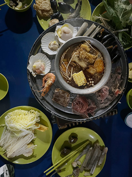 一桌丰盛的热气腾腾的火锅盛宴，摆满了各种海鲜、蔬菜和肉类，摆放在色彩鲜艳的桌子上，随时准备享用图片下载