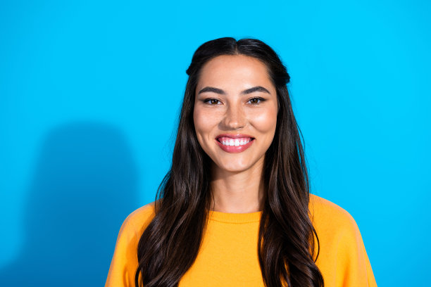 一位年轻的混血黑发女子穿着黄色毛衣，在蓝色背景前微笑，用于生活方式时尚图库照片图片下载