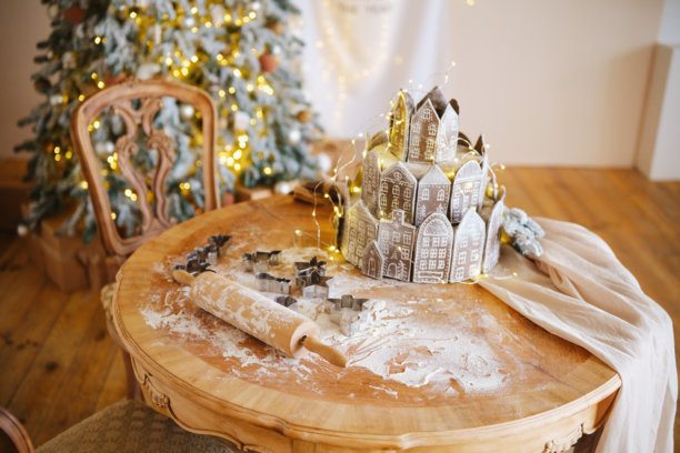 质朴的桌子上摆放着姜饼村庄和饼干模具，背景是节日灯饰和圣诞树图片下载