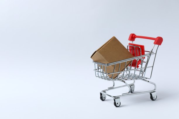 白色背景上的小型购物车的特写照片，上面放着一个纸板箱。购物概念。图片下载