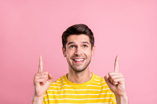照片：乐观的金发千禧一代男性，穿着黄色T恤，指向空白处，背景为粉色图片下载
