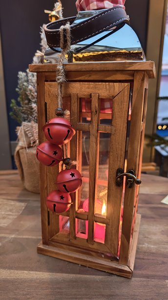 一张节日室内场景的图片，桌子上放着一盏带有发光蜡烛和红色金属铃铛的木制装饰灯笼。概念是圣诞气氛、舒适的冬季装饰和传统的节日温馨。图片下载