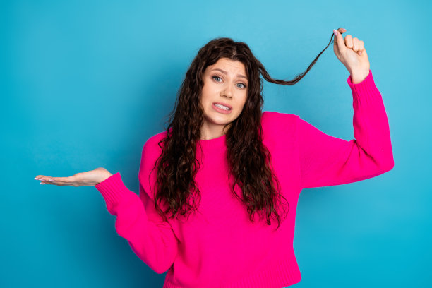 身穿粉色针织衫的年轻女子，摆出俏皮姿势，头发飘动，背景为蓝色，生活时尚素材图图片下载