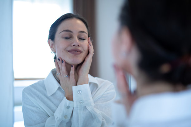 一位女性闭着眼睛，在镜子前享受她的护肤日常。此为素材图片。图片下载