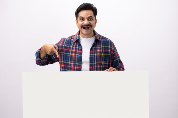 英俊的中年男子穿着格子衬衫，躲在空白的白墙后面，在白色背景下拍摄的素材照片图片下载